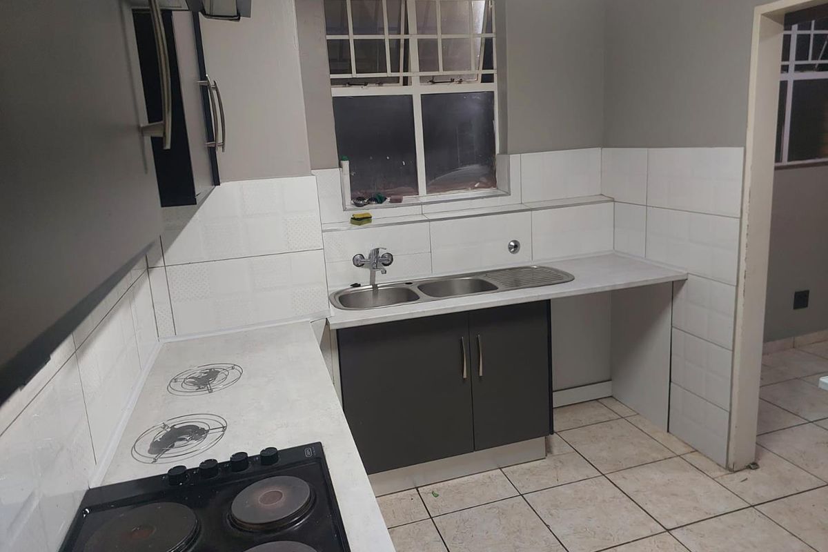 A functional kitchen featuring dark cabinetry, a built-in electric hob, double sink, and tiled splashbacks with tiled flooring.