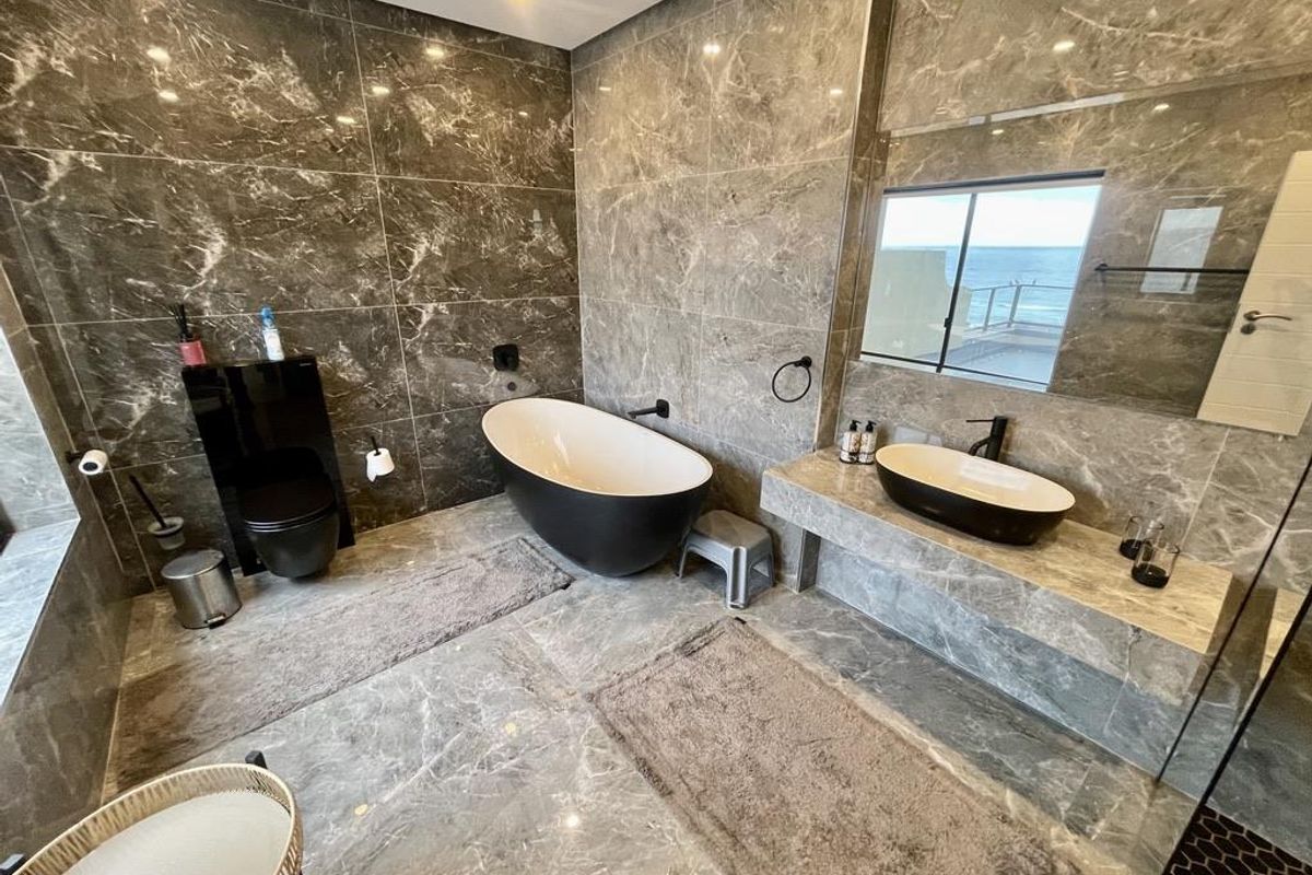 Modern bathroom featuring floor-to-ceiling marble tiling, a freestanding bathtub, a floating stone vanity with a vessel sink, and a wall-mounted toilet.