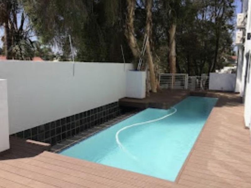 A private swimming pool area featuring modern timber decking, a clean boundary wall, and integrated air conditioning units on the building exterior.