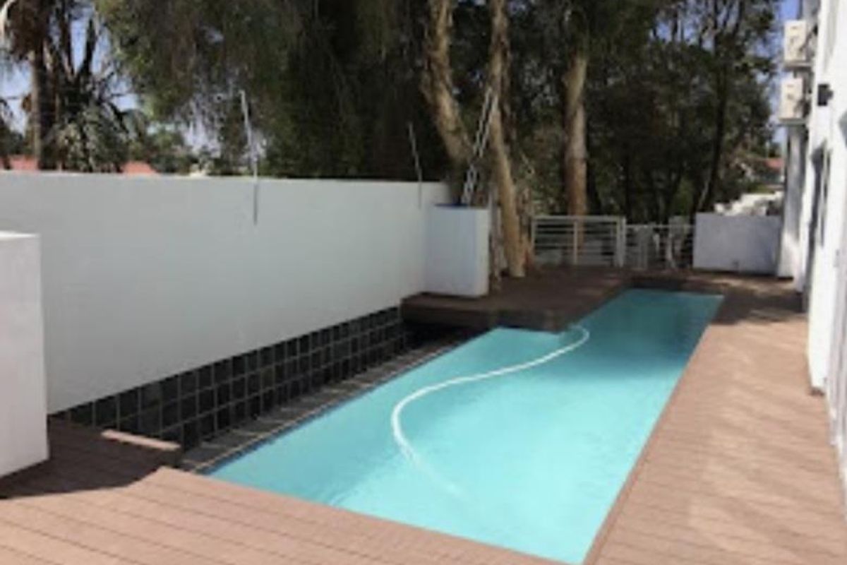 A private swimming pool area featuring modern timber decking, a clean boundary wall, and integrated air conditioning units on the building exterior.