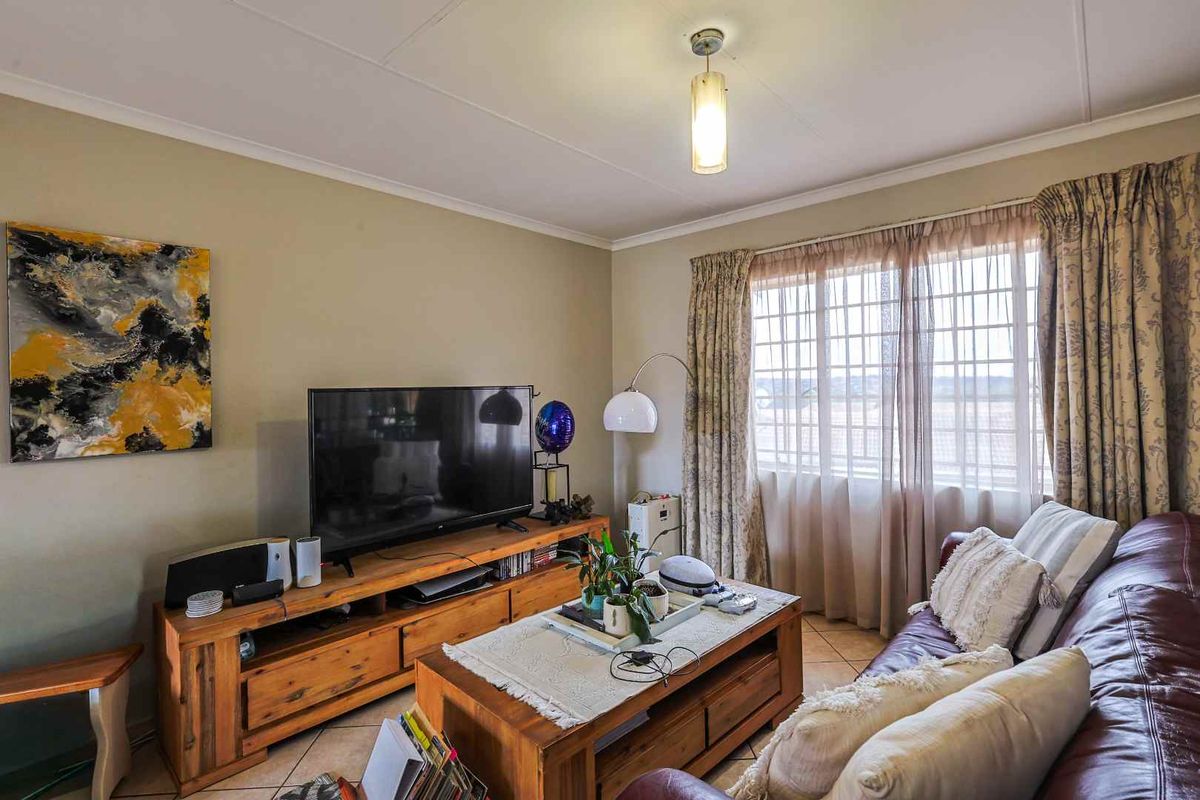 A comfortable living room featuring tiled flooring, large windows with security bars, and neutral wall finishes.