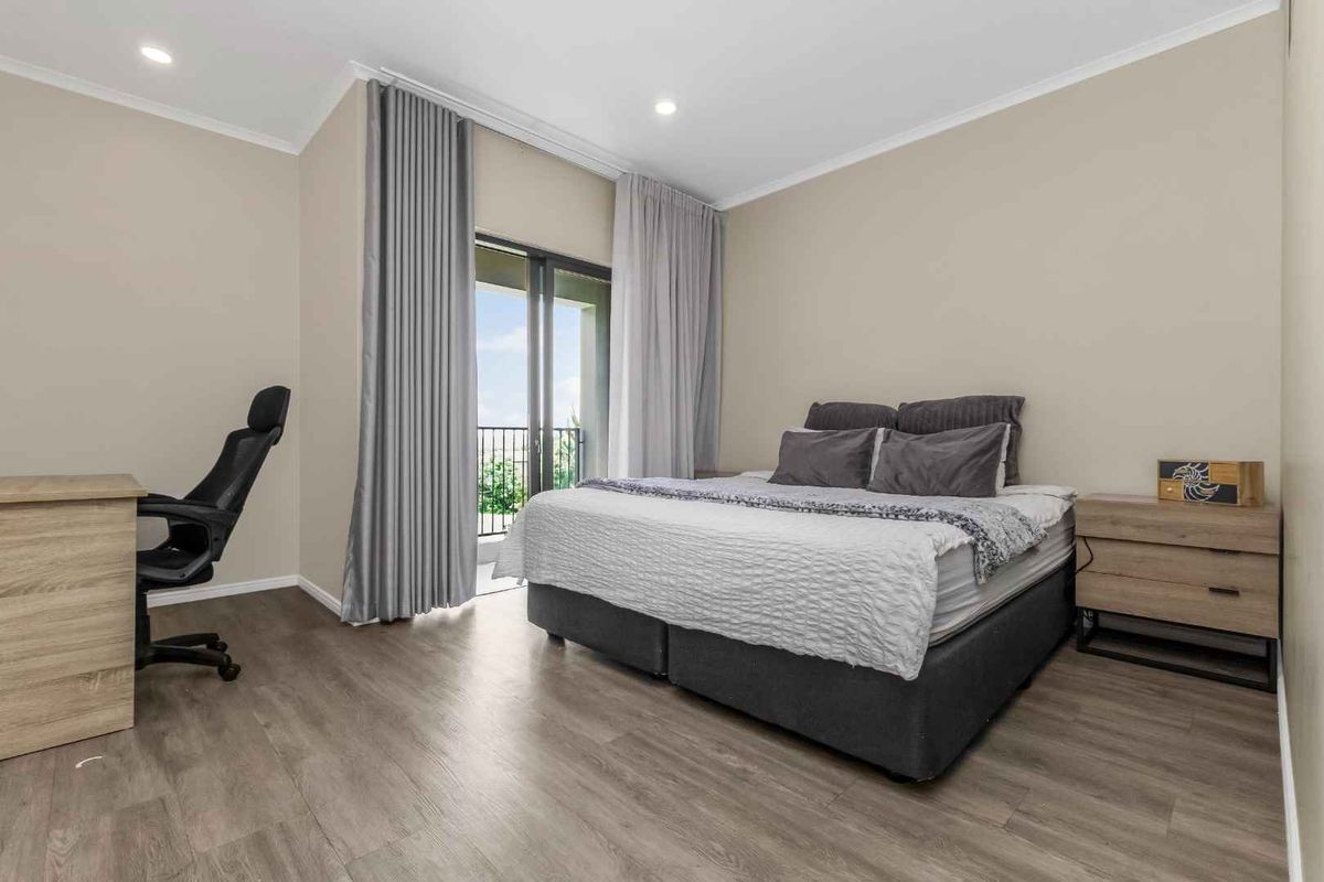 A well-maintained bedroom featuring modern laminate flooring, recessed lighting, and a sliding glass door providing direct access to a private balcony.