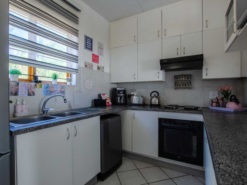 Functional kitchen featuring white cabinetry, granite-look laminate countertops, built-in oven, electric hob, extractor fan, and tiled backsplash with a double sink.