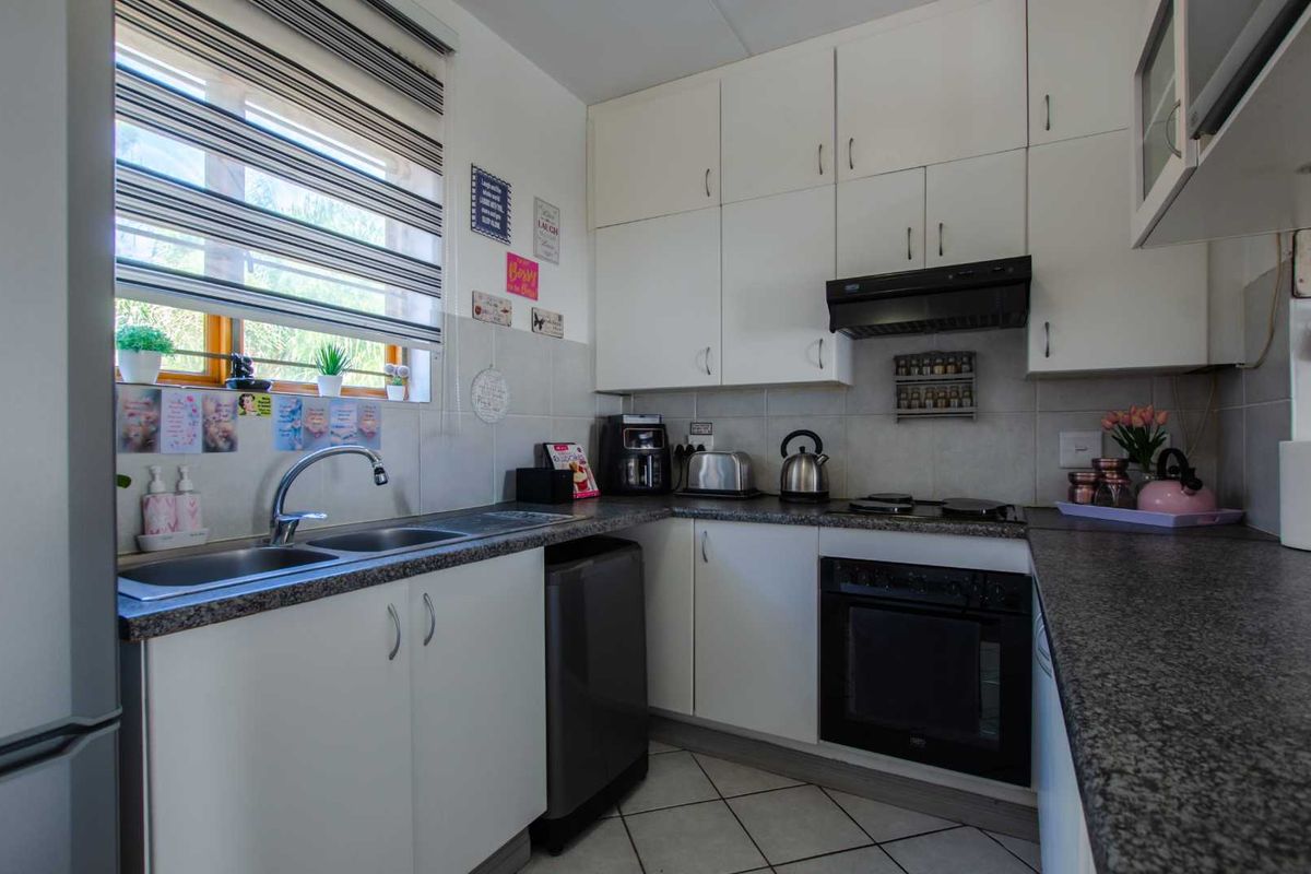 Functional kitchen featuring white cabinetry, granite-look laminate countertops, built-in oven, electric hob, extractor fan, and tiled backsplash with a double sink.