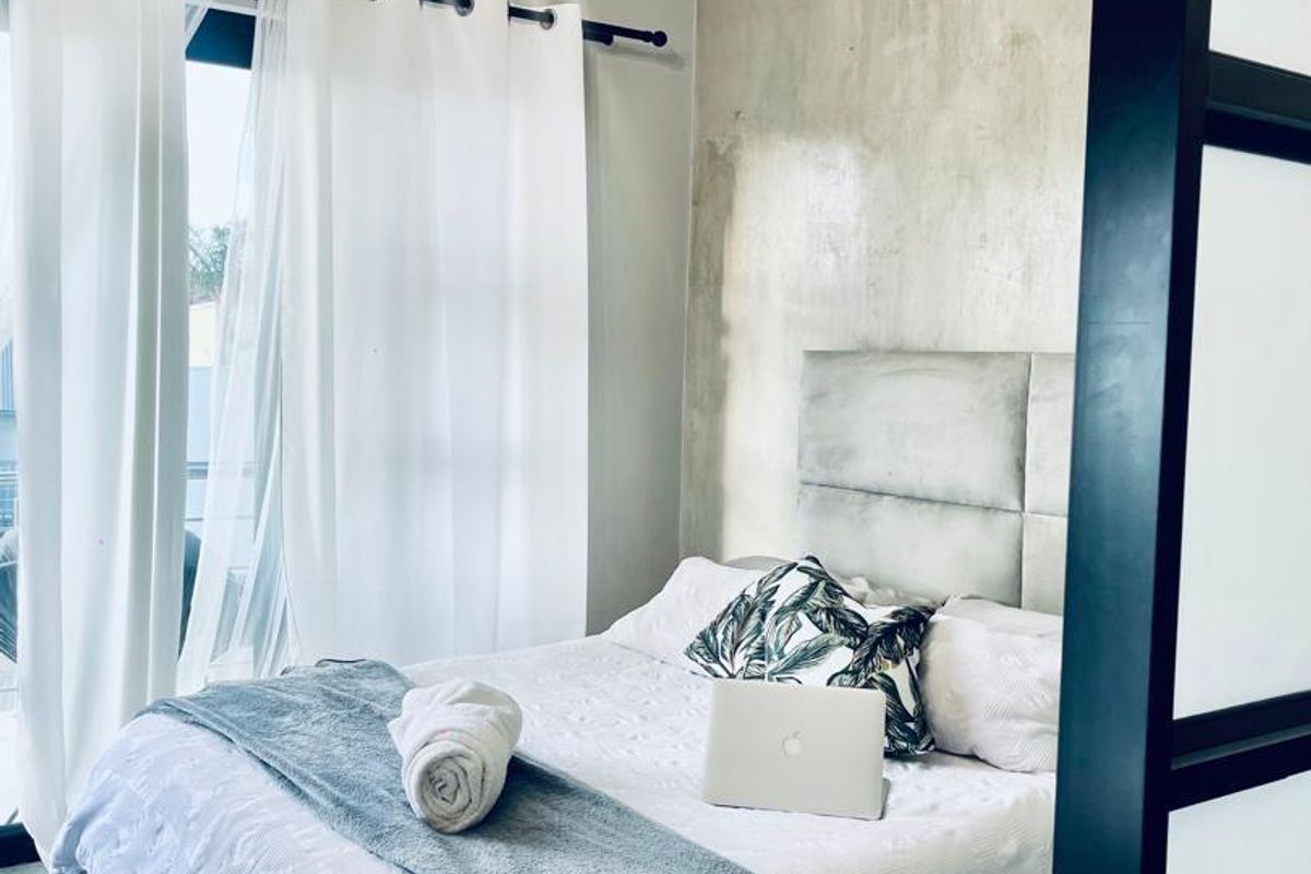 A modern bedroom featuring a concrete accent wall, upholstered headboard, and pendant lighting, with direct access to an outdoor area through sliding glass doors.