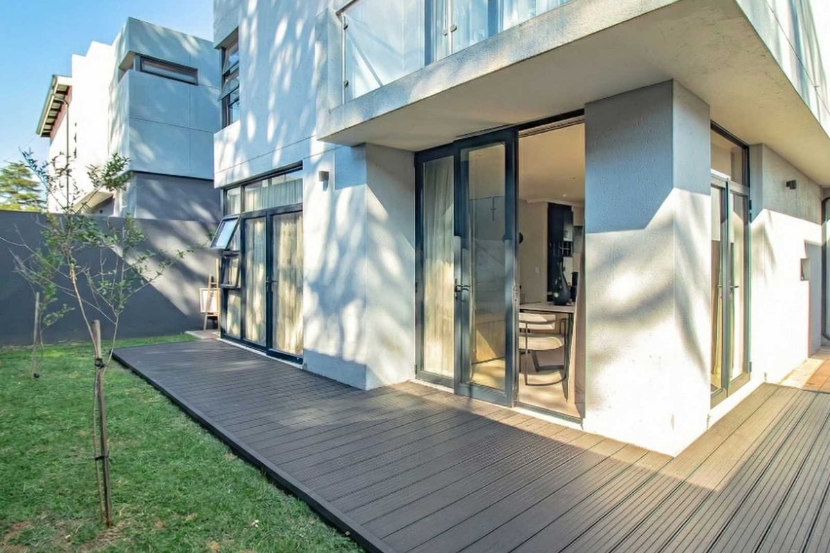 A modern rear exterior view featuring a composite deck, landscaped garden, and large glass sliding doors leading into the living area.