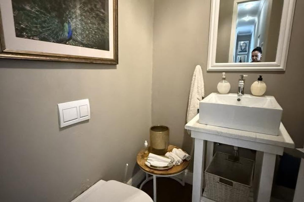 A compact guest bathroom featuring a wall-mounted toilet, a modern vessel sink on a wooden vanity stand, and a framed wall mirror.