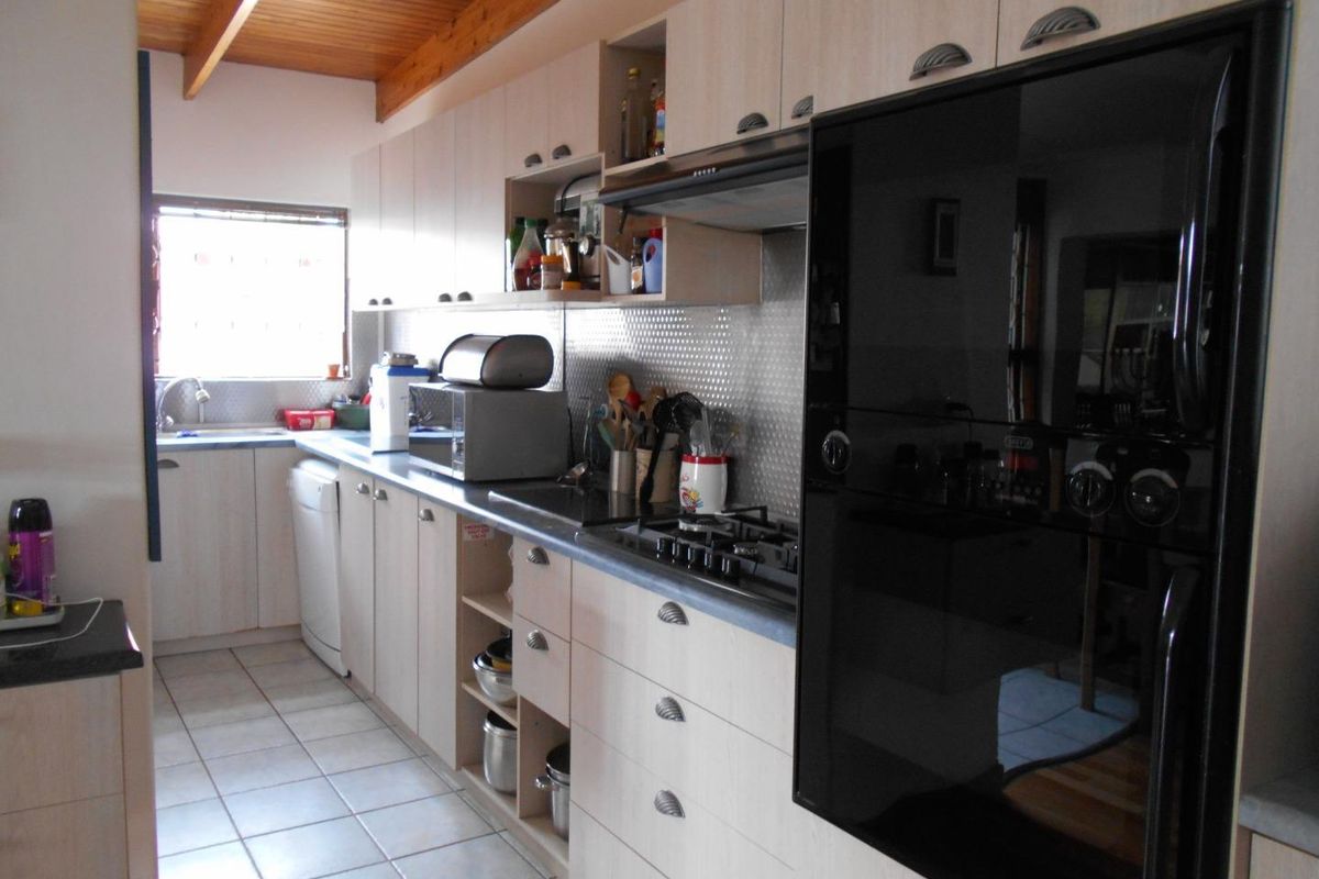 A functional kitchen featuring light wood cabinetry, a built-in oven, gas hob, extractor fan, and tiled flooring under a timber-beamed ceiling.