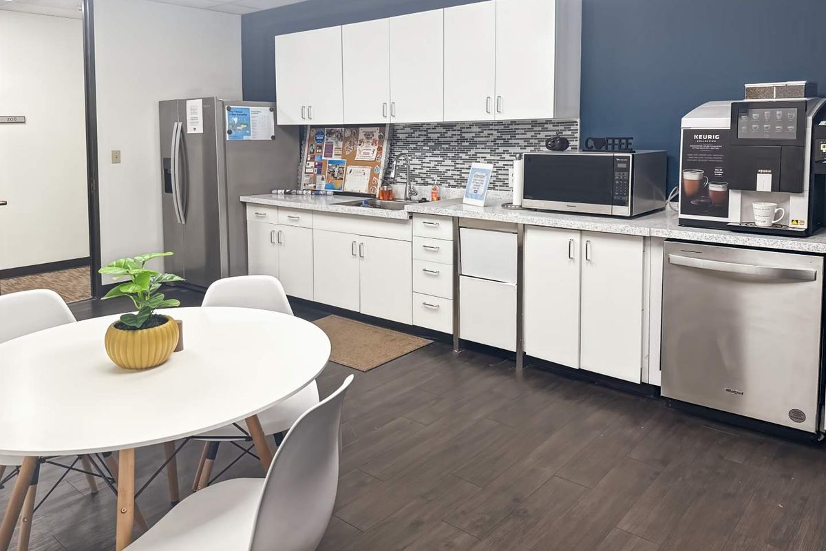 A functional office kitchenette featuring white cabinetry, a mosaic tile backsplash, laminate countertops, and integrated stainless steel appliances.