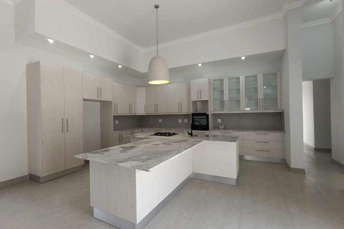 Modern kitchen featuring light-toned cabinetry, stone countertops, a central island with a built-in hob, and integrated oven, set in a spacious open-plan layout.
