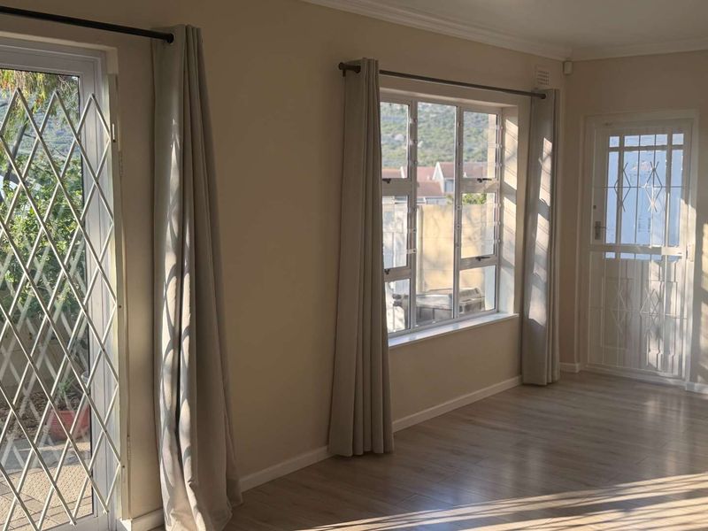 Bright and spacious living area featuring laminate flooring, large windows with security gates, and neutral wall finishes.