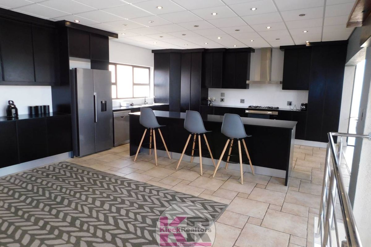 Modern kitchen featuring dark built-in cabinetry, a central island, stainless steel extractor fan, and tiled flooring with recessed lighting throughout.