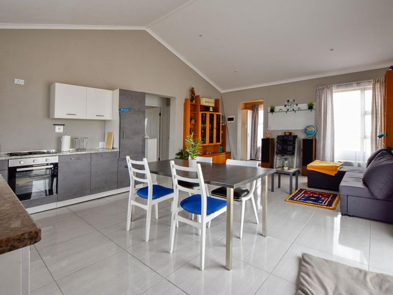 Open-plan living area featuring a modern kitchen with built-in oven and hob, tiled flooring, and a spacious vaulted ceiling.