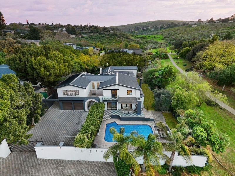 Aerial view of a modern residential property featuring a swimming pool, paved driveway, double garage, and landscaped surroundings in a scenic location.