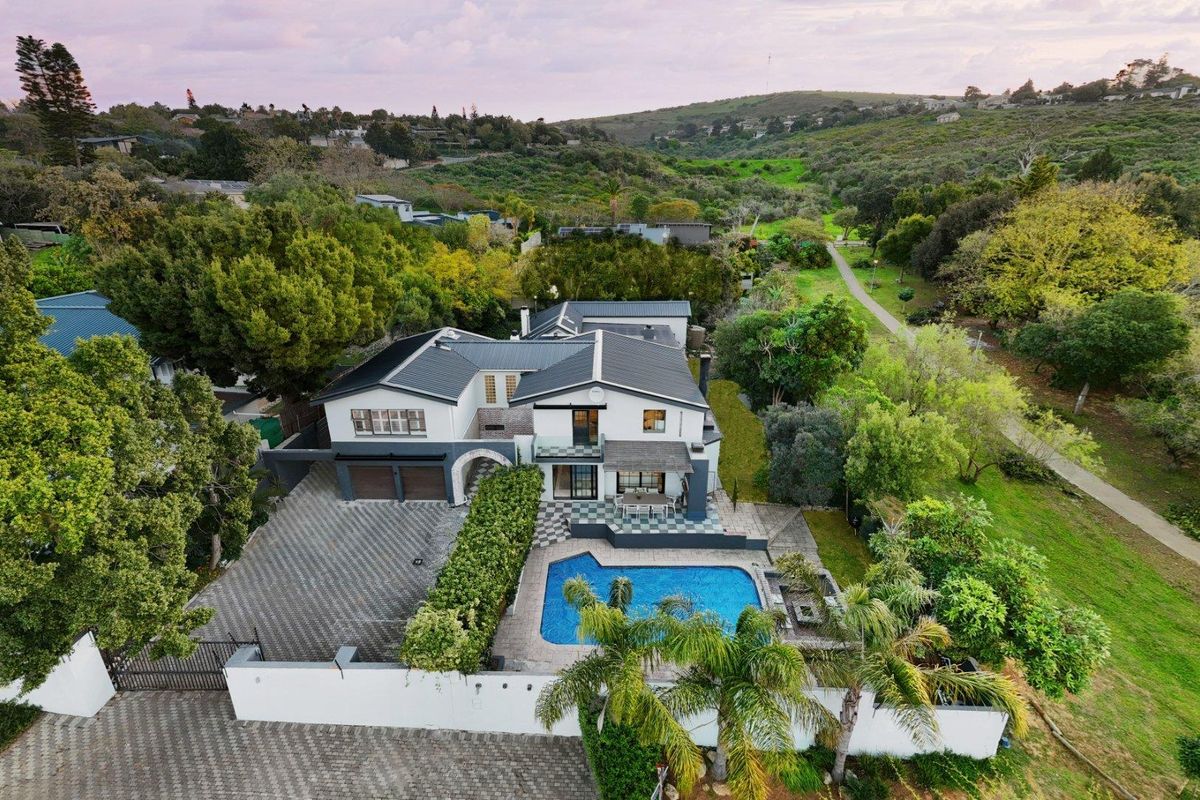 Aerial view of a modern residential property featuring a swimming pool, paved driveway, double garage, and landscaped surroundings in a scenic location.