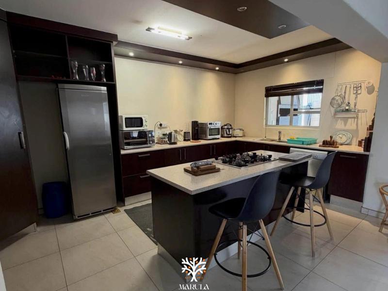 Modern kitchen featuring dark wood cabinetry, a central island with a gas hob, stone countertops, and recessed ceiling lighting.