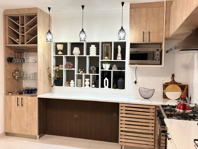 Modern kitchen featuring light wood cabinetry, built-in microwave, gas hob, extractor fan, and integrated wine storage with stylish open shelving.
