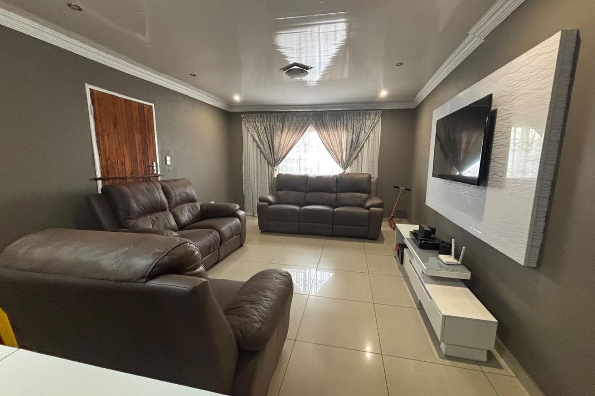 A spacious living room featuring large format floor tiles, a glossy ceiling finish, and a modern built-in media wall unit.