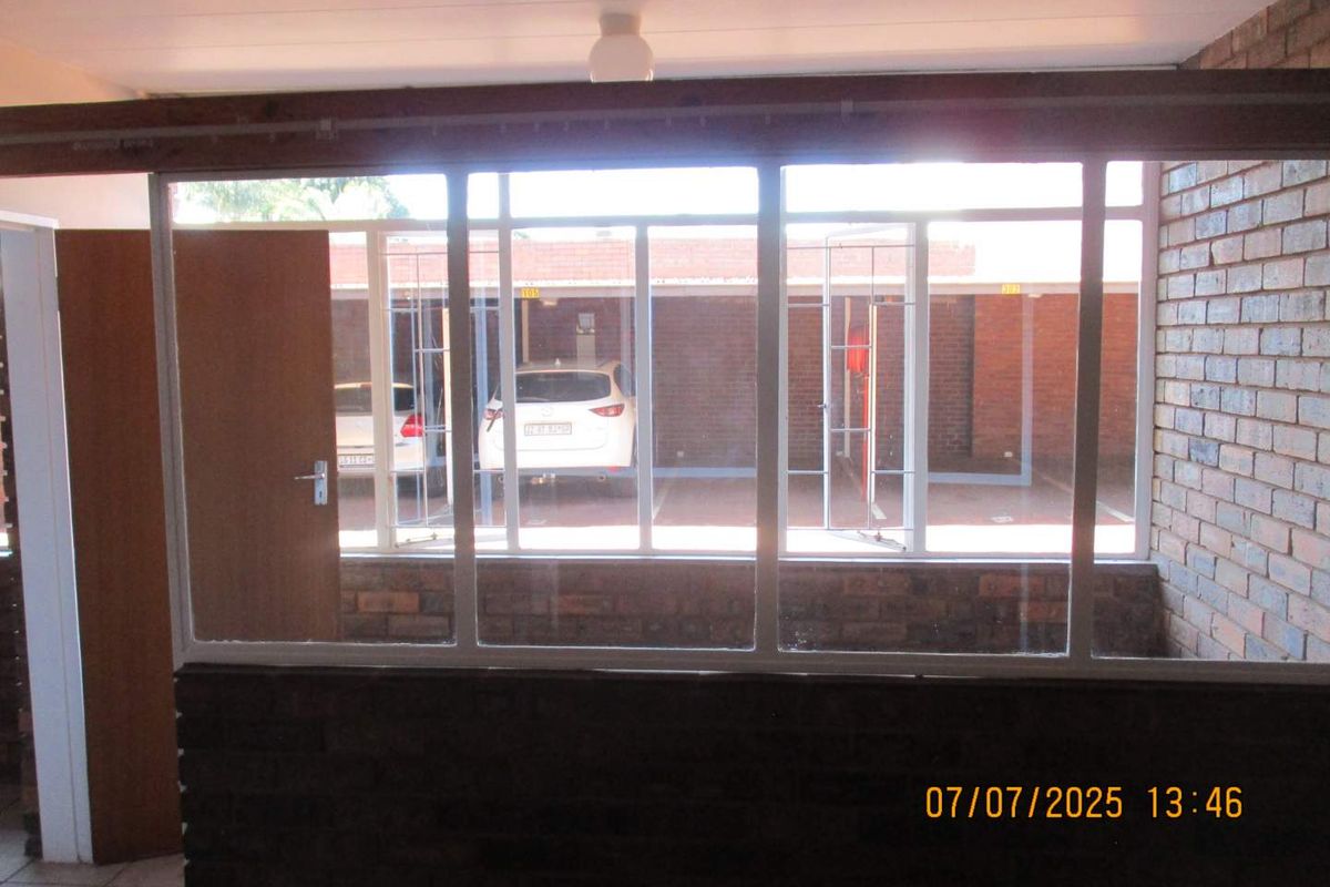An interior view looking out through a large window partition towards a covered parking area with brick wall finishes.