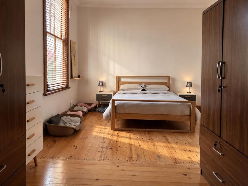 A well-maintained bedroom featuring warm timber flooring, natural light through venetian blinds, and classic coving detail.