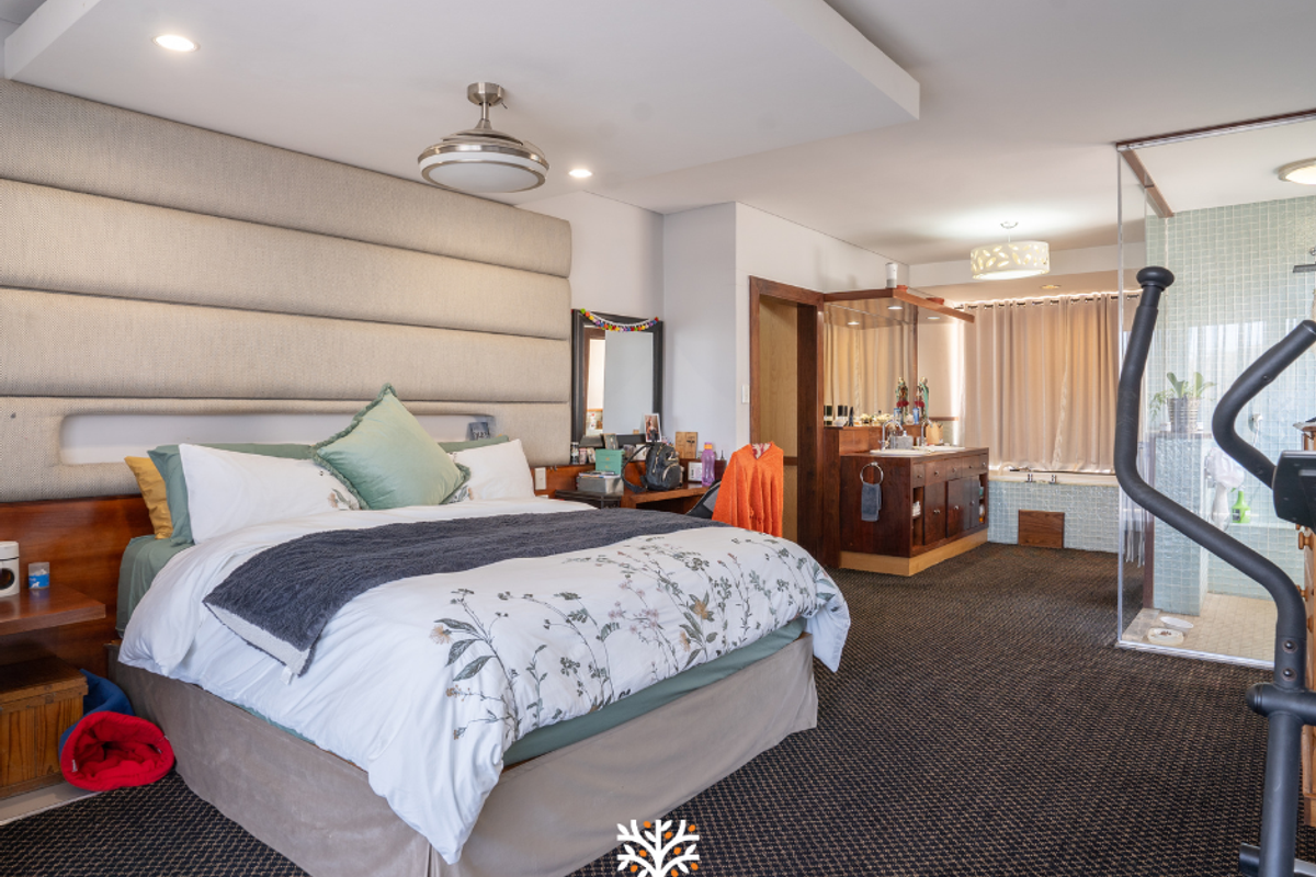 Spacious bedroom featuring a large upholstered headboard, integrated vanity area, and an open-plan en-suite bathroom with a glass-enclosed shower and soaking tub.