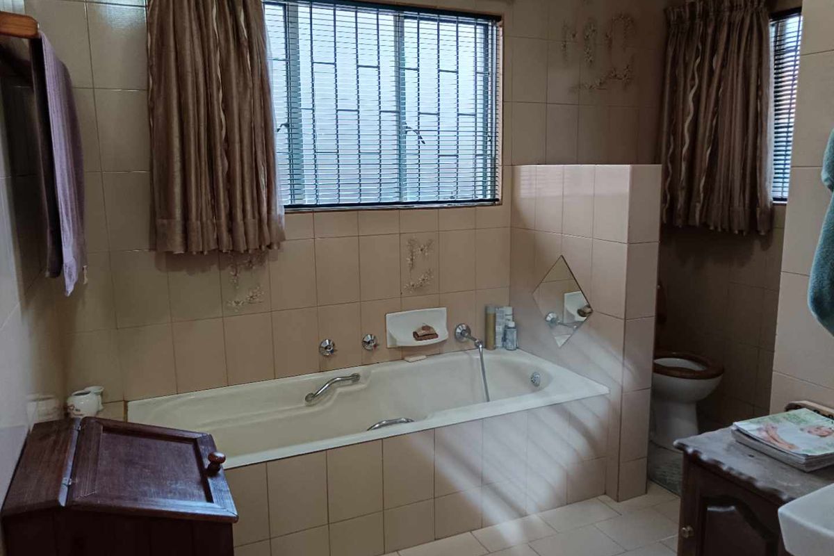 A dated bathroom featuring a built-in bathtub, tiled walls, and a separate toilet area with security bars on the window.