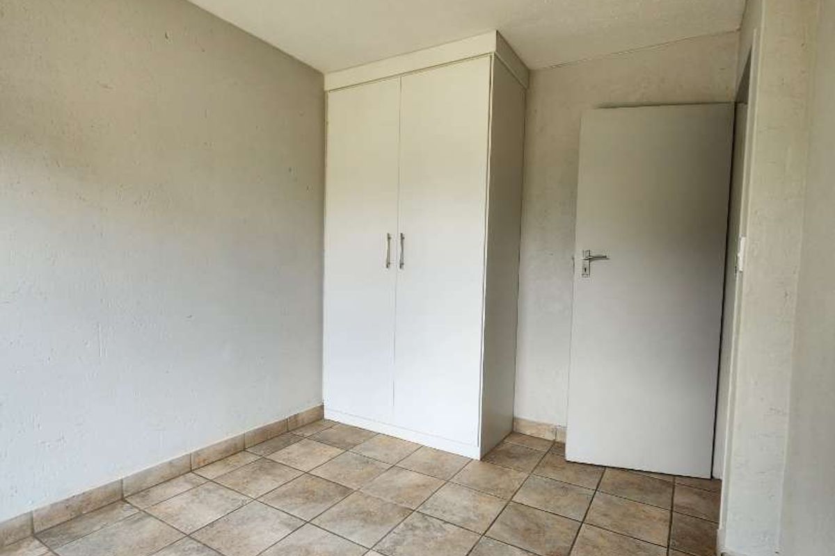 A vacant bedroom featuring tiled flooring, a built-in wardrobe, and neutral wall finishes, offering a clean canvas for personalization.