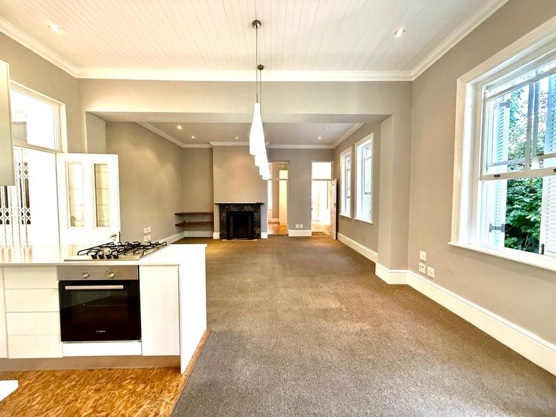 Spacious open-plan living area featuring a modern kitchen island with built-in oven and gas hob, fireplace, and large sash windows.