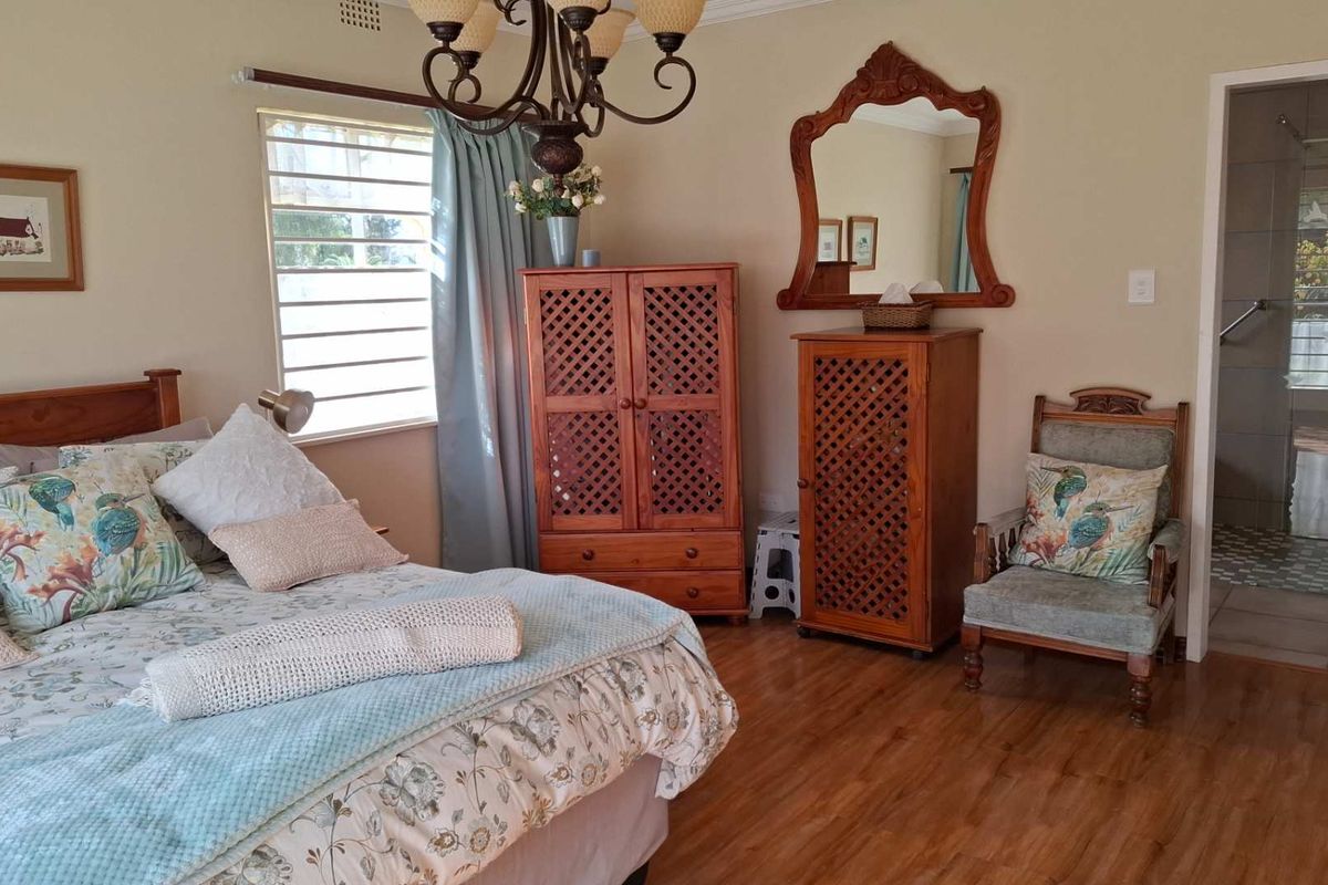 A well-maintained bedroom featuring laminate flooring, a ceiling-mounted light fixture, and an en-suite bathroom with a glass-enclosed shower.