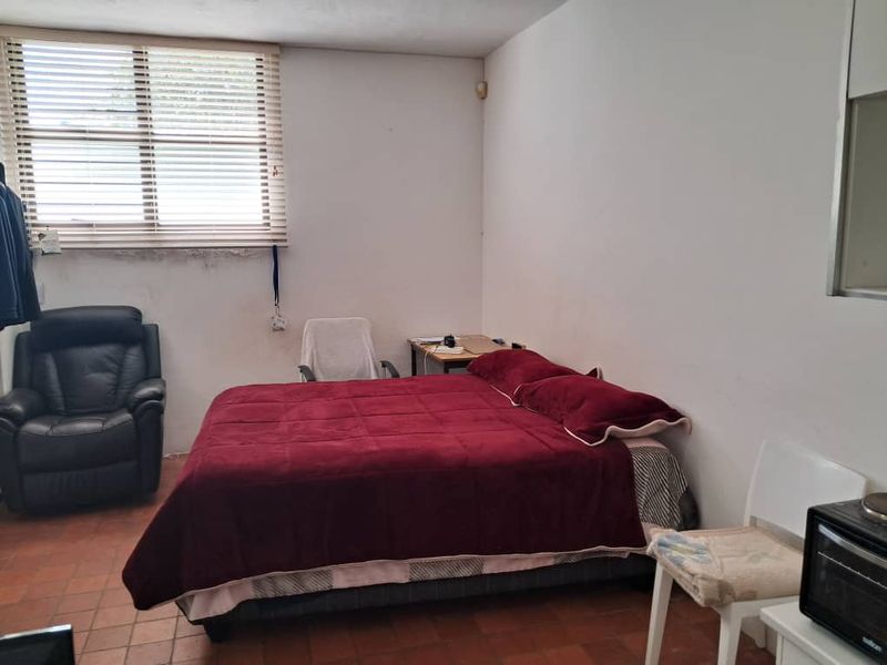 A bedroom featuring terracotta floor tiles and a window with venetian blinds, showing signs of wall wear and staining.