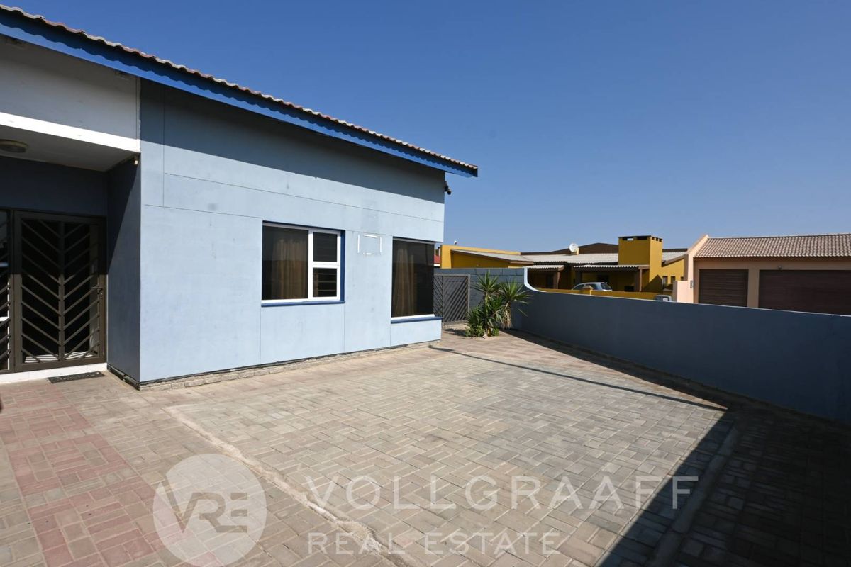 A paved rear courtyard area featuring a boundary wall and access to the main house structure.