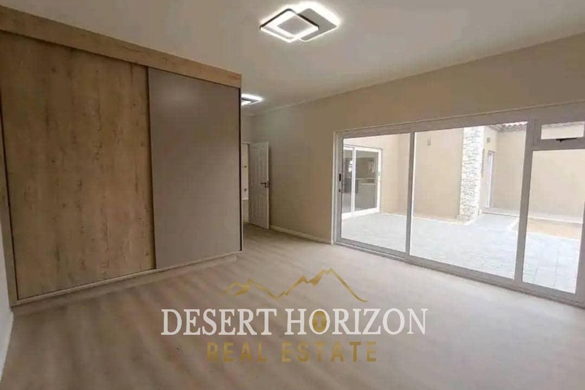 A bright, modern bedroom featuring built-in wardrobes, laminate flooring, and large sliding glass doors providing access to an outdoor patio area.