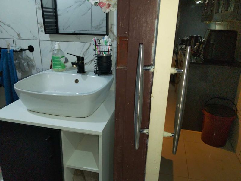 A compact bathroom featuring a modern vessel sink, vanity cabinet, and marble-look wall tiles, adjacent to a doorway with a worn frame.