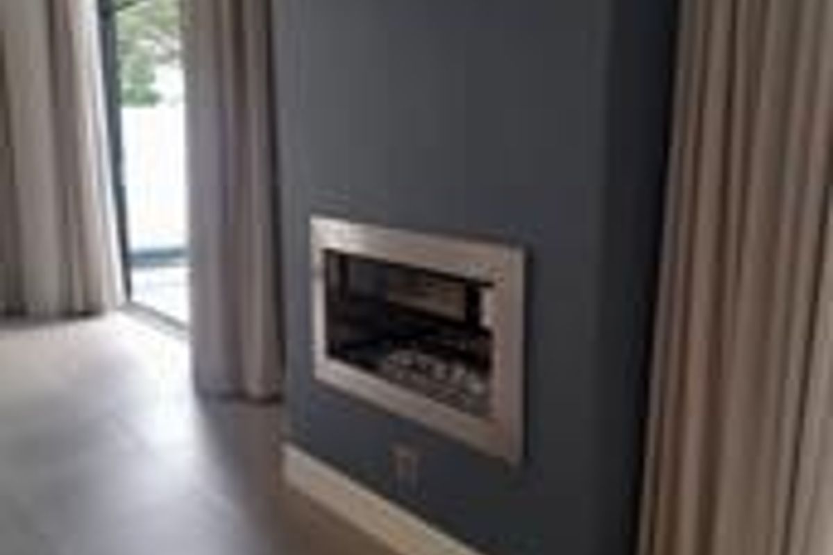A modern living room featuring a sleek built-in fireplace set into a feature wall, with large windows and tiled flooring.