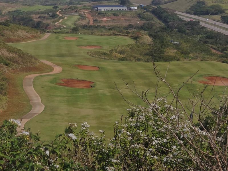 Elevated view overlooking a well-maintained golf course fairway with sand bunkers and a winding paved cart path.