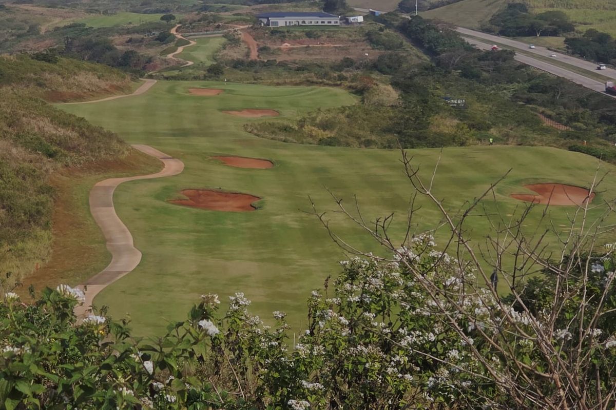 Elevated view overlooking a well-maintained golf course fairway with sand bunkers and a winding paved cart path.