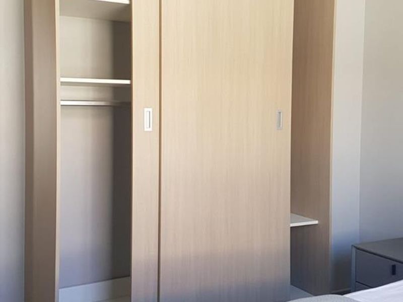 A bedroom featuring a modern, light-wood finish built-in wardrobe with sliding doors and integrated shelving.