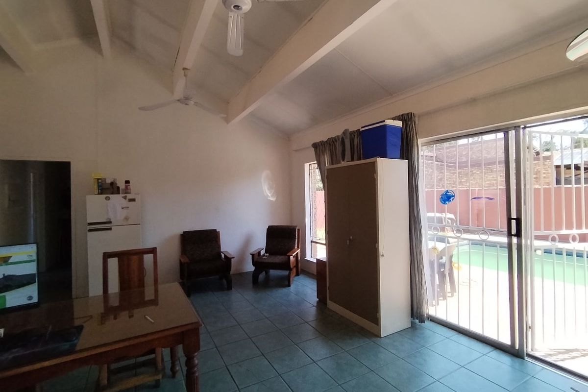 Spacious living area featuring vaulted ceilings, ceiling fans, and tiled flooring, with direct access to the pool area through sliding glass doors.