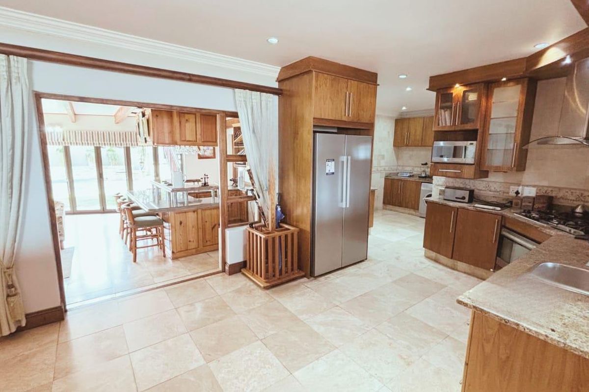 Spacious kitchen featuring wooden cabinetry, granite countertops, integrated appliances, and tiled flooring, with an open-plan flow leading to an adjacent dining area.