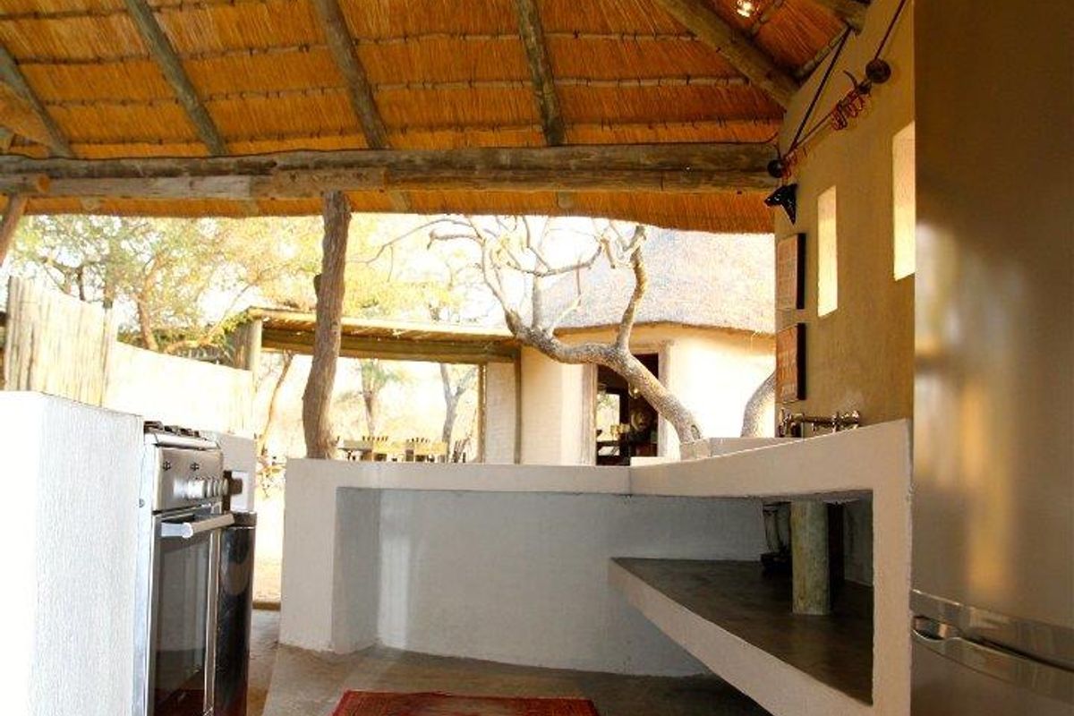 An open-air kitchen area featuring a thatched roof, built-in masonry counters, and a stainless steel stove.