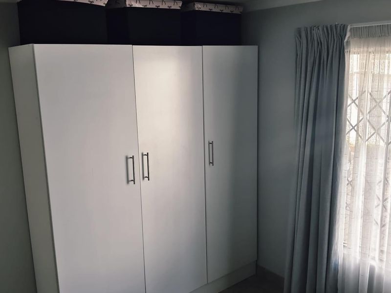 A bedroom featuring a white built-in wardrobe, tiled flooring, and a window fitted with a security gate and curtains.