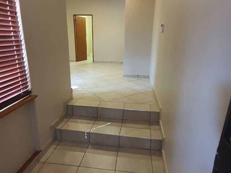 A clean, tiled hallway featuring recessed downlighting and a step leading to an adjacent room, providing a neutral transition space.