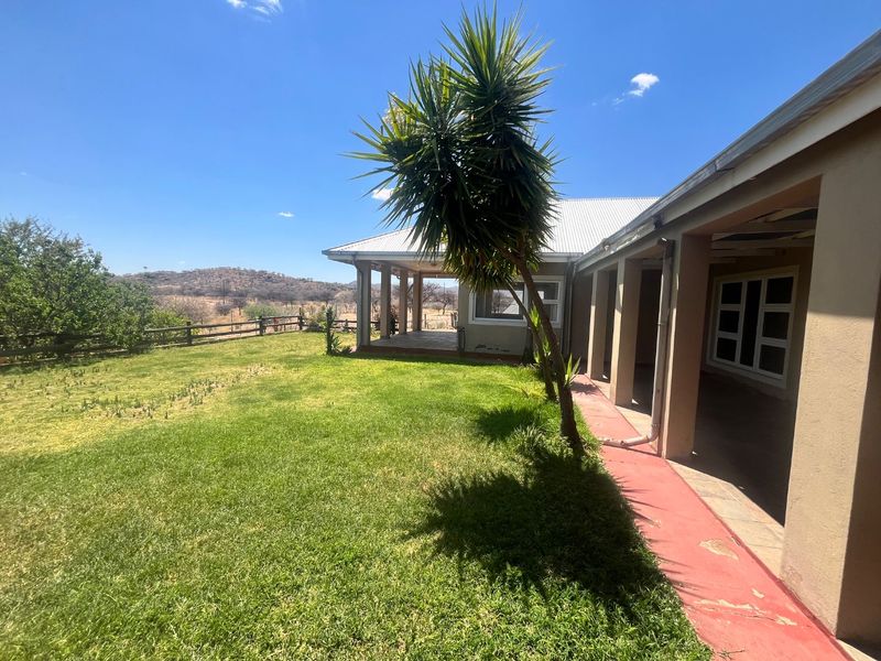Rear view of the property featuring a covered patio, a spacious lawn, and a concrete walkway with scenic landscape views.