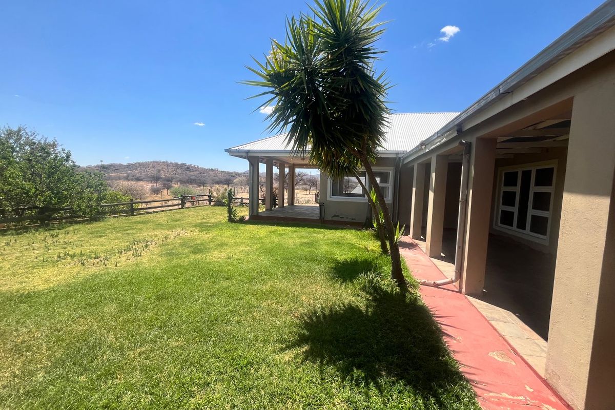 Rear view of the property featuring a covered patio, a spacious lawn, and a concrete walkway with scenic landscape views.