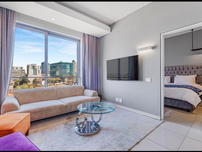 Modern living room featuring large sliding glass doors with city views, neutral tiled flooring, and recessed ceiling lighting, leading into an adjacent bedroom.
