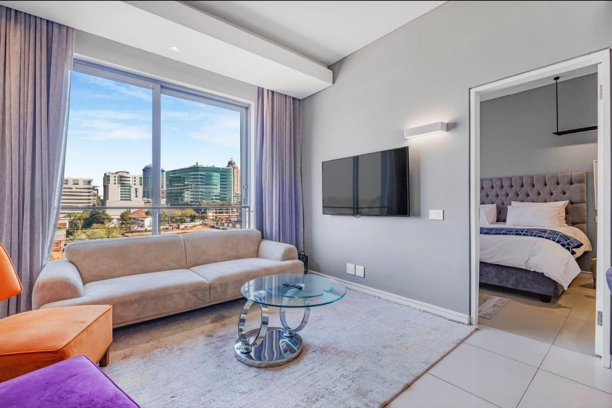 Modern living room featuring large sliding glass doors with city views, neutral tiled flooring, and recessed ceiling lighting, leading into an adjacent bedroom.