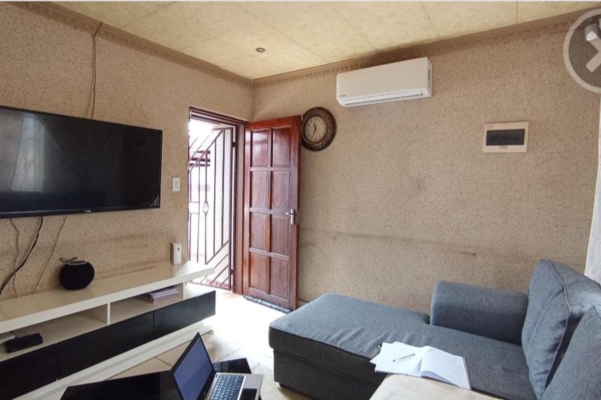 A living room featuring tiled floors, an air conditioning unit, and direct access to an exterior area through a timber door with a security gate.