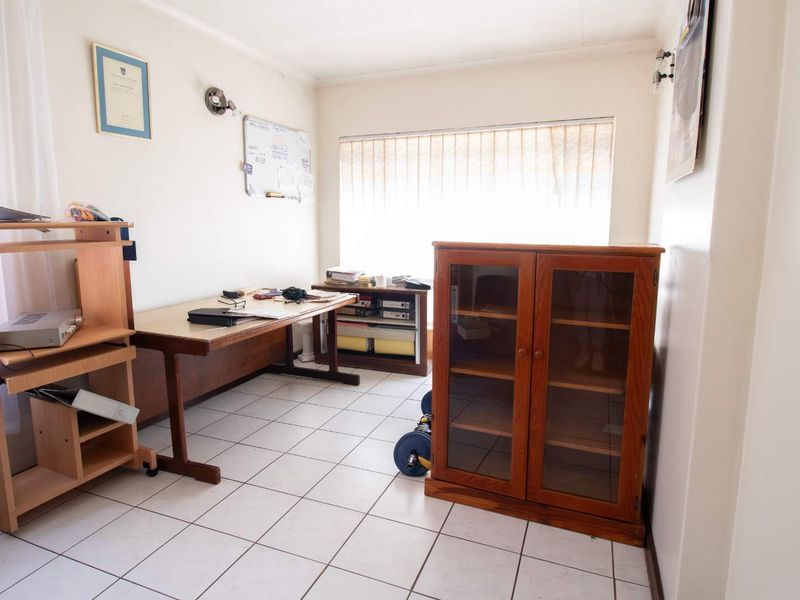 A functional home office space featuring tiled flooring and vertical blinds, providing a practical area for work or study.