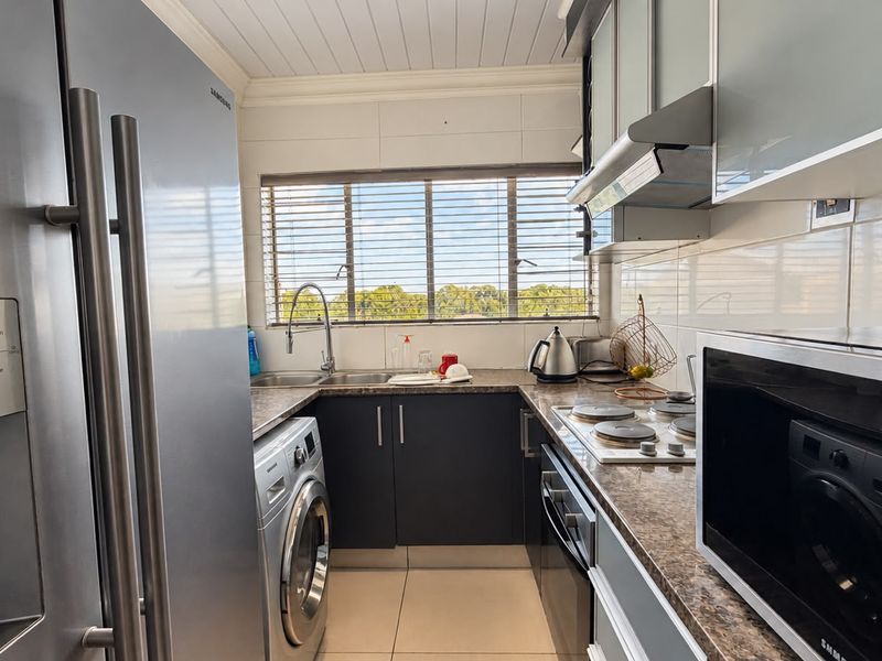A functional kitchen featuring dark cabinetry, granite-look countertops, built-in oven and hob, and integrated laundry appliances, finished with a clean tiled splashback.