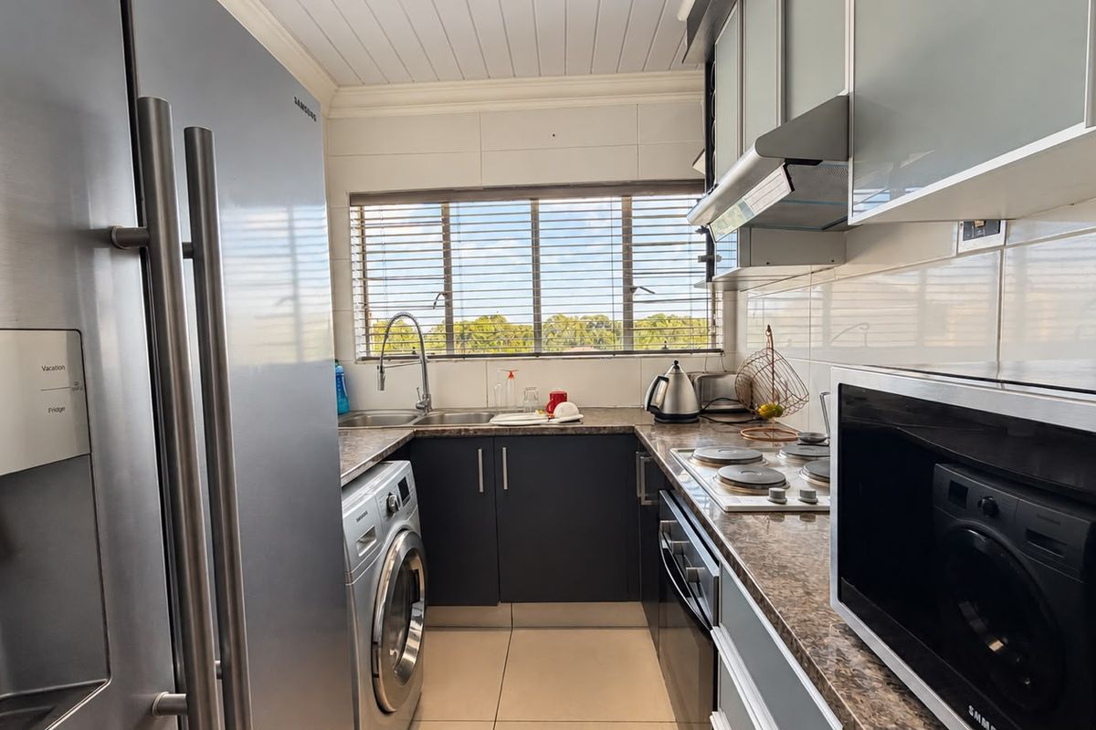 A functional kitchen featuring dark cabinetry, granite-look countertops, built-in oven and hob, and integrated laundry appliances, finished with a clean tiled splashback.